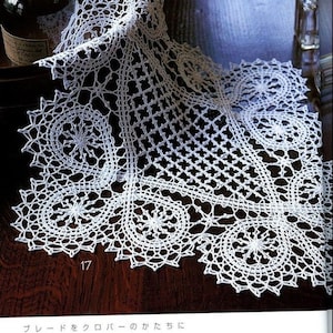 Puede incluir: Un camino de mesa de crochet blanco con un delicado patrón de encaje. El camino de mesa está doblado por la mitad y tiene un borde festoneado. El camino de mesa mide 42 cm por 54 cm.