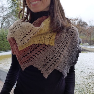 Può includere: Uno scialle all'uncinetto con un gradiente di colori, tra cui beige, giallo, arancione e marrone. Lo scialle ha un motivo traforato e un bordo a scalare.