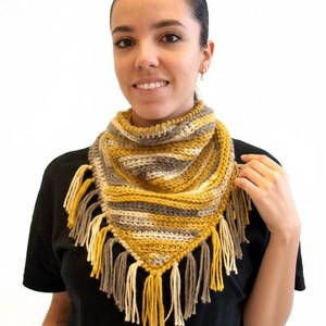 Puede incluir: Un pa&ntilde;uelo bandana triangular de ganchillo con rayas horizontales en amarillo mostaza, gris y crema. El accesorio est&aacute; rematado con largos y gruesos flecos de lana en los mismos tonos amarillo mostaza, gris y crema en el borde inferior.