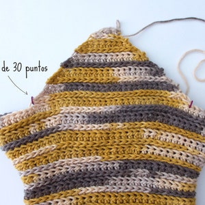 Puede incluir: Una pieza de ganchillo en forma de estrella tejida con hilo matizado en rayas horizontales de color amarillo mostaza, gris y crema. Dos peque&ntilde;os marcadores de puntos morados est&aacute;n sujetos a los bordes, con texto que se&ntilde;ala "Marcador de 30 puntos".