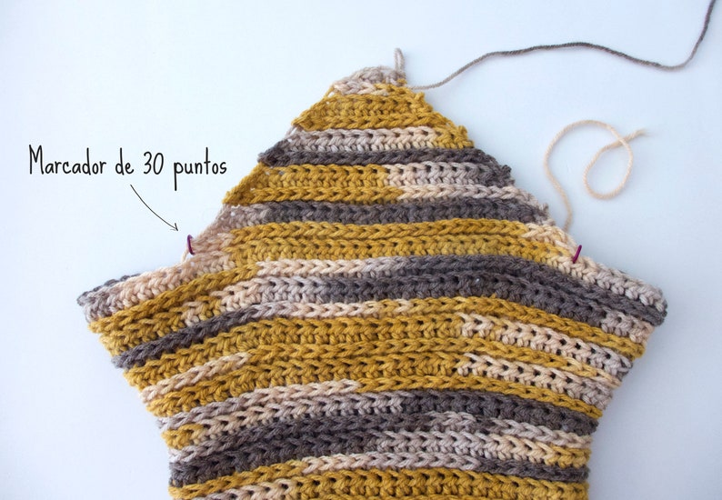 Puede incluir: Una pieza de ganchillo en forma de estrella tejida con hilo matizado en rayas horizontales de color amarillo mostaza, gris y crema. Dos peque&ntilde;os marcadores de puntos morados est&aacute;n sujetos a los bordes, con texto que se&ntilde;ala "Marcador de 30 puntos".