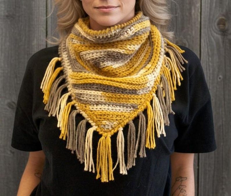 Puede incluir: Un pa&ntilde;uelo triangular de ganchillo con un patr&oacute;n variado de hilo amarillo mostaza, crema y topo. El accesorio tiene una textura acanalada y est&aacute; rematado con largos y gruesos flecos de hilo a lo largo de los bordes inferiores y la punta.