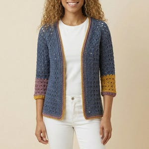 May include: A blue open-front crochet cardigan featuring three-quarter length sleeves with contrasting mustard yellow and mauve cuffs. The garment has a textured, open-stitch pattern throughout and is worn over a plain white t-shirt and white jeans.