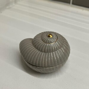 May include: A gray ceramic seashell trinket box with a gold accent on the top.