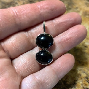 May include: A silver pendant with two black round stones. The stones are set in silver and the pendant has a silver bail.