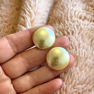 May include: A pair of round, yellow-green, iridescent earrings. The earrings are smooth and have a pearlescent finish.