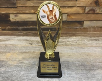 May include: A gold trophy with a round top featuring a goat with the text "Head Goat". The base of the trophy is black with a gold plate that says "Personalize Your Engraving Here!"
