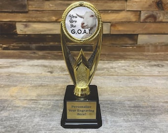 May include: A gold trophy with a black base. The trophy features a circular image of a goat with the text "You Are The G.O.A.T." The base has a plaque that reads "Personalize Your Engraving Here!"