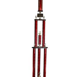 Op de afbeelding: Een hoge trofee met een rood en goud ontwerp. De trofee heeft meerdere niveaus, met een gouden figuur aan de bovenkant en een zwart bord. De trofee is ongeveer 122 cm hoog.