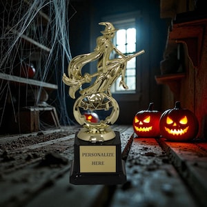 May include: A gold-colored Halloween trophy featuring a witch riding a broom over a carved pumpkin. The trophy sits on a black base with a gold plate that reads "PERSONALIZE HERE". Two lit jack-o'-lanterns are in the background.