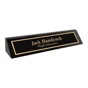 Puede incluir: Placa de escritorio negra con borde dorado, con el nombre "Jack Handcock" y el título "Flight Instructor" en letras doradas. La placa está en ángulo y tiene un acabado brillante.