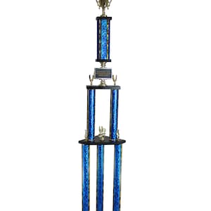 Puede incluir: Un trofeo alto con una base negra y columnas azules. El trofeo tiene múltiples niveles, con una copa dorada y una figura alada en la parte superior. El trofeo tiene una placa que dice "ENGRAVED TEXT OR GARY PLAQUE".