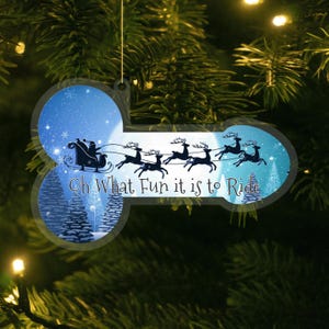 May include: A festive Christmas tree ornament with a winter scene. It depicts Santa's sleigh and reindeer, with the words "Oh What Fun it is to Ride". The ornament is suspended from a Christmas tree.