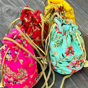 May include: A collection of colorful drawstring pouches in shades of pink, red, yellow, and teal. Each pouch is adorned with intricate floral embroidery and gold-colored cord drawstrings, creating a vibrant and ornate aesthetic. The pouches are likely used for carrying small items.