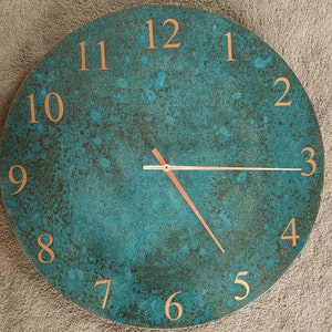 May include: A circular wall clock with a teal and copper finish. The clock face has a textured appearance with copper-coloured numerals and hands. The clock measures approximately 30 cm in diameter.