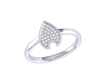 May include: A silver-toned ring featuring a pointed, shield-shaped centerpiece. The face of the shield is inlaid with a cluster of small, clear, sparkling stones arranged in a grid pattern, set against a smooth, polished metallic band.