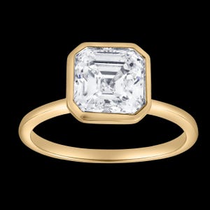 May include: A gold ring featuring a square-cut, clear, faceted gemstone set in a smooth, polished bezel setting. The band is a simple, solid gold hoop with a rounded profile, providing a clean and uniform appearance to the jewelry piece.