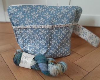 May include: A blue and white floral zippered pouch with a clear plastic window and a blue and white yarn skein with a label that reads "Hedge Row Yarns".