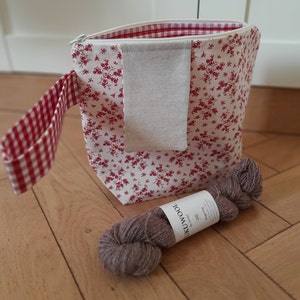 May include: A red and white gingham fabric zippered pouch with a small pocket and a floral print. The pouch is filled with a skein of brown yarn with a label that reads "Lukuwool by Lucy" and "fingering".