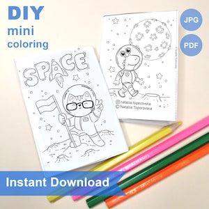 Puede incluir: Dos cuadernillos de papel blanco con dibujos de líneas en blanco y negro para colorear, con ilustraciones de temática espacial de un gato y un dinosaurio con trajes de astronauta en la luna, acompañados de cuatro lápices de colores.