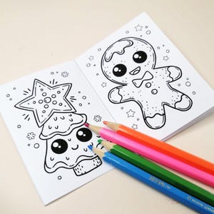 Könnte beinhalten: Ein Malbuch zum Thema Weihnachten mit einem Lebkuchenmann- und Weihnachtsbaum-Design. Das offene Buch wird von einem Satz farbiger Bleistifte in Blau, Grün, Pink und Orange begleitet.