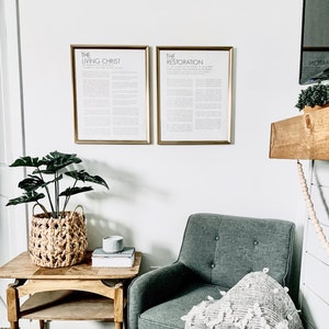 Puede incluir: Un sillón gris con una manta blanca se encuentra en una sala de estar con una mesa auxiliar de madera y una planta en maceta. Dos impresiones enmarcadas con el texto "The Living Christ" y "The Restoration" cuelgan de la pared.