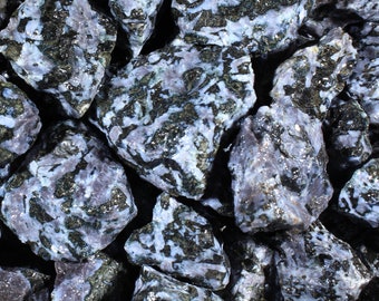 May include: A collection of rough, tumbled stones. The stones have a mix of colors, including dark blue, black, and white. The stones have a speckled appearance and a slightly glossy finish. The overall theme is natural and earthy.