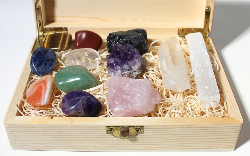 May include: A wooden box filled with a variety of crystals and stones, including amethyst, rose quartz, clear quartz, selenite, and agate. The box is lined with wood shavings and has a brass latch.