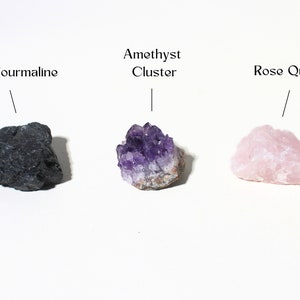 May include: Three different types of crystals: a black tourmaline, an amethyst cluster, and a rose quartz.