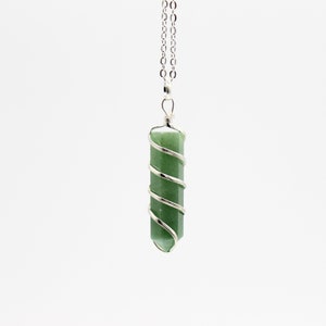 May include: A green gemstone pendant necklace. The pendant is a cylindrical shape, wrapped with a silver-colored wire in a spiral design. The necklace chain is also silver-colored and hangs against a white background.