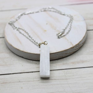 May include: A white selenite crystal pendant on a silver chain necklace. The pendant is a rectangular shape and is about 2 inches long.