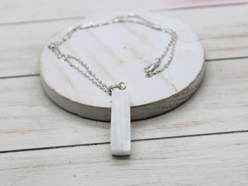 May include: A white selenite crystal pendant on a silver chain necklace. The pendant is a rectangular shape and is about 2 inches long.