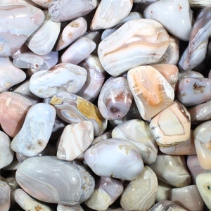 May include: A collection of smooth, polished agate stones in shades of white, gray, and pink with intricate banding patterns.