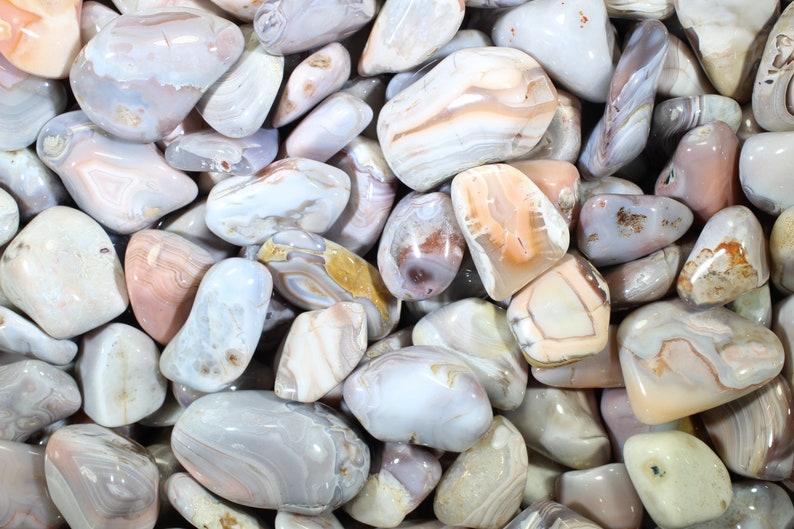 May include: A collection of smooth, polished agate stones in shades of white, gray, and pink with intricate banding patterns.