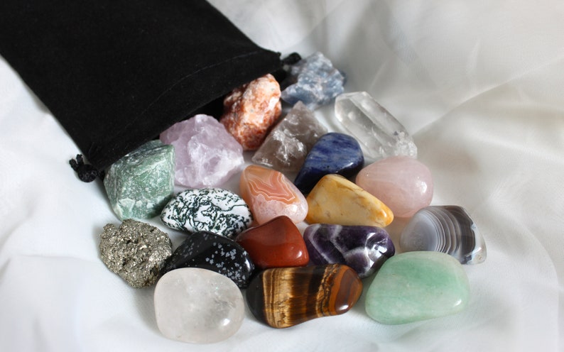 May include: A collection of tumbled stones in a variety of colors and textures, including amethyst, rose quartz, tiger's eye, and clear quartz. The stones are arranged in a loose pile on a white fabric background.