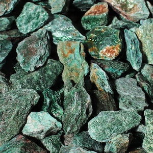 May include: Close-up of a pile of rough-cut, green stones. The stones vary in size and shape, with a mix of textures and shades of green, some with hints of brown. The stones appear to be natural and unpolished.