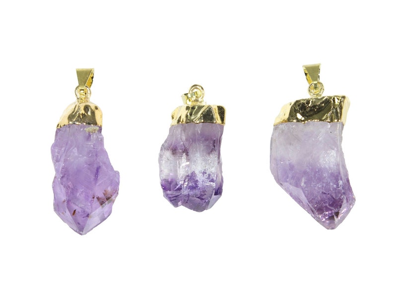 K&ouml;nnte beinhalten: Drei Amethyst-Kristall-Anh&auml;nger mit vergoldeten Oberteilen. Die Kristalle sind roh und haben einen violetten Farbton.