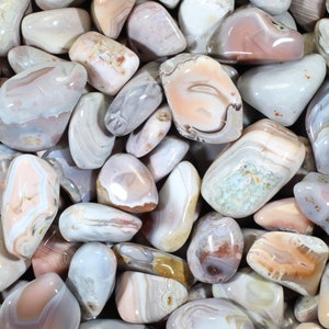 May include: A collection of tumbled agate stones in shades of pink, white, and gray. The stones have a variety of patterns and textures.