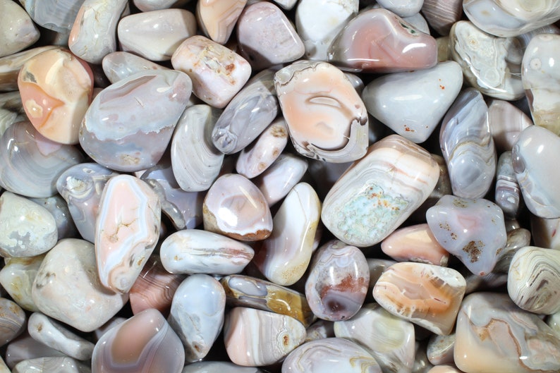 May include: A collection of tumbled agate stones in shades of pink, white, and gray. The stones have a variety of patterns and textures.