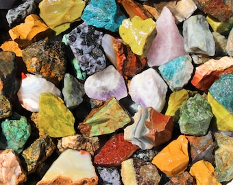 May include: A collection of colorful, rough-cut gemstones, including amethyst, agate, jasper, and turquoise. The stones are various sizes and shapes, and some have a natural, polished finish.