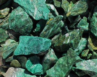 May include: A close-up of a pile of green and white jade stones. The stones are rough and have a natural, unpolished look.