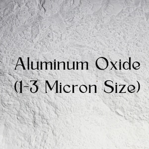 May include: A close-up image of a white, textured surface. The text "Aluminum Oxide (1-3 Micron Size)" is displayed in black, centered on the image. The background has a mottled appearance.