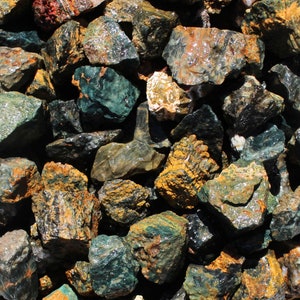 May include: A close-up of a pile of green and yellow jasper stones. The stones are rough and have a natural, unpolished finish.