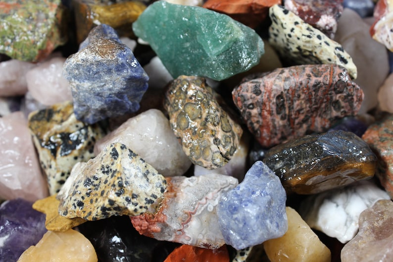 May include: A collection of various colorful gemstones and rocks. The image showcases a variety of shapes, sizes, and colors, including green, blue, red, white, and speckled patterns. The gemstones appear to be natural and unpolished.