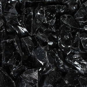 Puede incluir: Primer plano de un mont&oacute;n de rocas de obsidiana negras, irregulares y brillantes. Las rocas tienen bordes afilados y una superficie reflectante, que atrapa la luz y crea reflejos. La textura general es &aacute;spera y fragmentada.