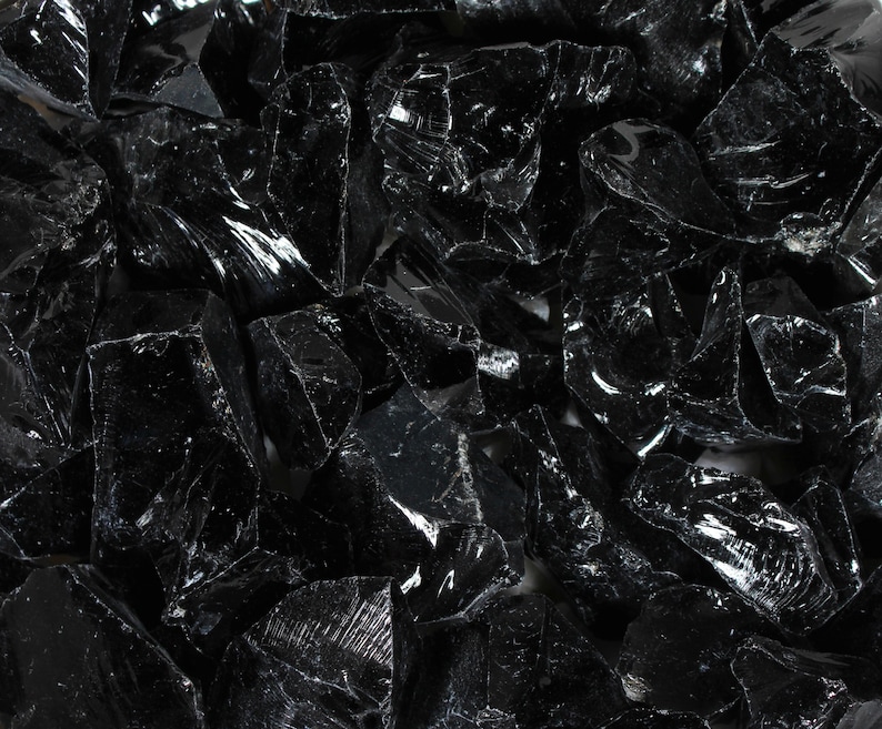 Puede incluir: Primer plano de un mont&oacute;n de rocas de obsidiana negras, irregulares y brillantes. Las rocas tienen bordes afilados y una superficie reflectante, que atrapa la luz y crea reflejos. La textura general es &aacute;spera y fragmentada.