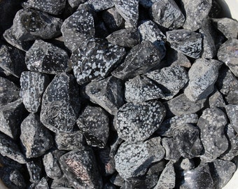 May include: A collection of black and white snowflake obsidian stones. The stones are rough and have a speckled appearance.