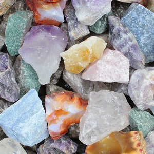 May include: A collection of rough, natural gemstones in various colors, including amethyst, clear quartz, green aventurine, and carnelian. The stones are tumbled and have a variety of shapes and sizes.