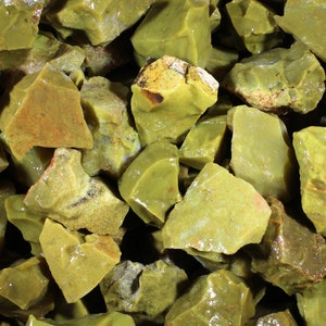 May include: A close-up of a pile of green opal rough stones. The stones are various sizes and shapes, with a translucent, glassy appearance.