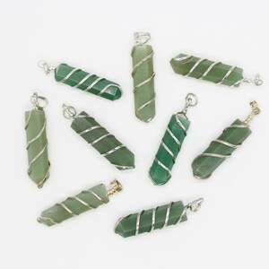 May include: A collection of green gemstone pendants with silver wire wrapping. Each pendant is a hexagonal shape with a loop at the top for a chain. The pendants vary slightly in shade, from light to dark green.